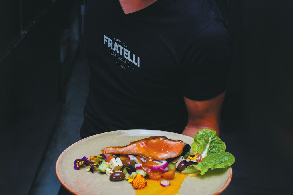 Fratelli waiter wearing a branded t-shirt and holding a plate of food. Italian restaurant branding and premium hospitality graphic design Melbourne