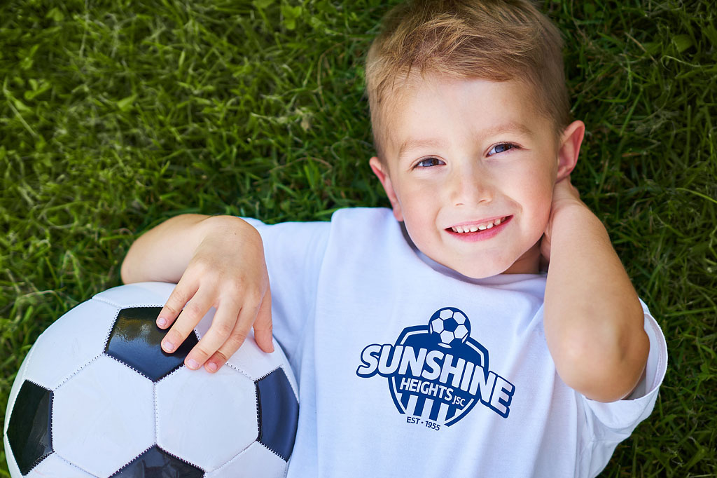 Young Sunshine Heights Junior Soccer Club player wearing branded club T-shirt while holding a soccer ball, showcasing community branding and sports club identity created by Melbourne freelance branding consultant.